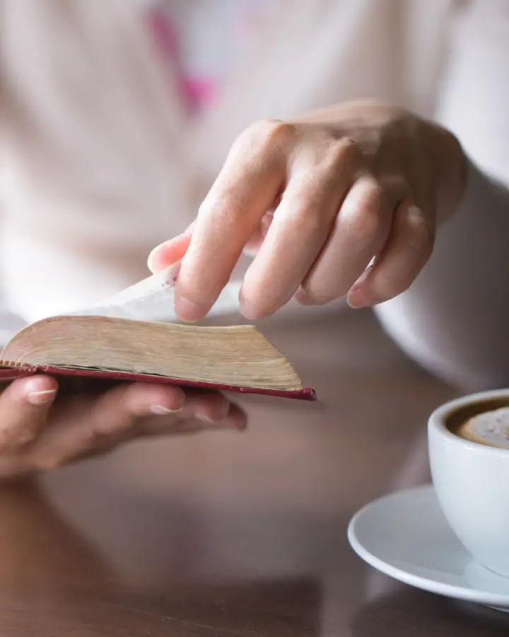 hand turning the page of bible with coffee cup nearby